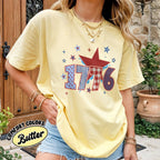 Person wearing a yellow t-shirt with '1776' design, standing outdoors.