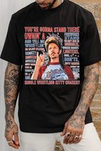 Person wearing a black t-shirt with a graphic and text, standing against a stone wall.