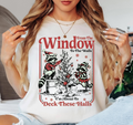 A woman wearing a white graphic t-shirt with a Christmas-themed raccoon design that reads 'From The Window To The Walls! I'm About To Deck These Halls'.
