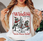 A woman wearing a white graphic t-shirt with a Christmas-themed raccoon design that reads 'From The Window To The Walls! I'm About To Deck These Halls'.